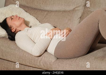 Donna matura di mezza età che soffre di mal di stomaco a casa. Dolore addominale, avvelenamento da cibo, diarrea, ulcera gastrica, dolore mestruale, menopausa. Foto Stock