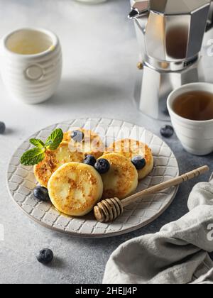 Frittelle di formaggio Syrniki o cottage con mirtillo e miele su piastra di ceramica Foto Stock