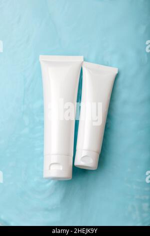 Prodotti cosmetici bianchi in tubetti su sfondo blu con gocce. Mock up Skincare cosmetici pacchetti sulla superficie dell'acqua. Acqua naturale idratante Foto Stock