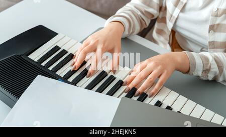 Donna che suona pianoforte registra la musica sul sintetizzatore usando appunti e laptop. Il pianista musicista delle mani femminili migliora le abilità di suonare il pianoforte. Musica online Foto Stock