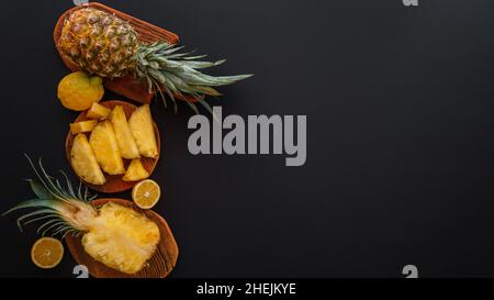 Ananas a fette in diverse forme. Ananas maturo sul tagliere che cucinano dessert estivo su sfondo nero. Disposizione piatta. Banner Web lungo con copia Foto Stock