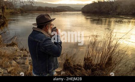 L'escursionista gode di uno splendido scenario naturale con una tazza di bevanda calda. Uomo che beve caffè e ammirare il bel fiume all'alba. Foto Stock