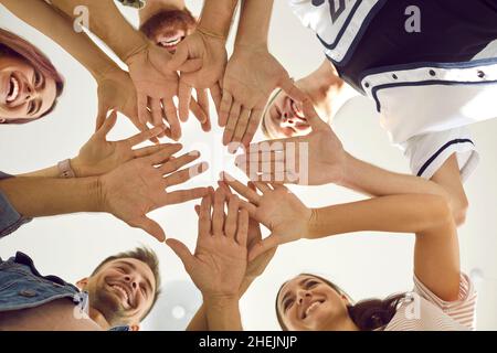 Vista dal basso di un gruppo di giovani felici e sorridenti che si mettono le mani insieme Foto Stock