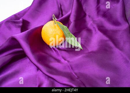 arancio mandarino con foglia verde, su una sciarpa viola satinata Foto Stock