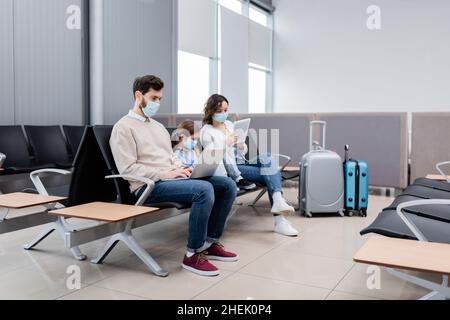 genitori maschere mediche utilizzando gadget vicino figlia in aeroporto Foto Stock