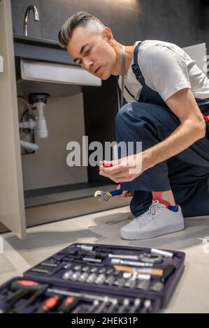 Uomo accovacciato vicino attrezzi che osservano il dettaglio in mano Foto Stock