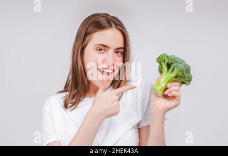 Donna che mostra broccoli. Cibo sano, vita di salute. Concetto di cibo crudo. Le mani di Womans che tengono mazzo di broccoli su sfondo grigio chiaro. Faccia ravvicinata Foto Stock