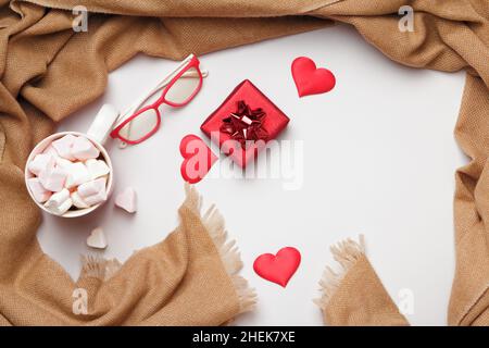 Composizione del giorno di San Valentino. Beige tazza sciarpa in cashmere marshmallows cuori bicchieri regalo su uno sfondo grigio. Foto Stock