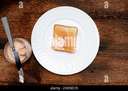 Sul pane tostato, pasta cremosa su un piatto bianco. Sfondo di legno scuro. Concetto di cibo. Uno spuntino veloce. Vista dall'alto. Foto Stock