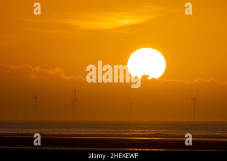 Ainsdale Beach, Southport, Merseyside, Regno Unito. 11th Jan 2022. Il sole si prepara a tramontare dietro turbine eoliche lontane mentre il cielo si allontano, con l'alta pressione che si muove e le condizioni nel Nord Ovest che saranno sistemate per tutta la settimana. Credit: Callum Fraser/Alamy Live News Foto Stock