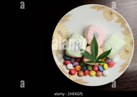 Dessert di cannabis. Delizia turca con fiocchi di cocco e confetti di caramelle colorate, vista dall'alto. Foglie verdi di cmarijuana su sfondo bianco della piastra. Layout Foto Stock