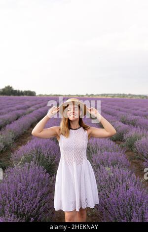 Una giovane bella signora si erge su un campo di lavanda in provenza, vestita con un abito bianco e un cappello di paglia. Foto Stock