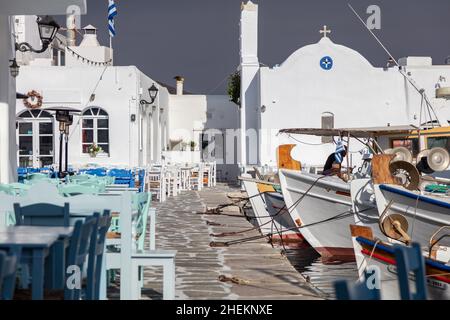 Grecia, Paros isola Naousa porto vecchio. Barca da pesca ormeggiata al molo del porto, tavolo da caffè e sedie all'aperto sul mare. Foto Stock