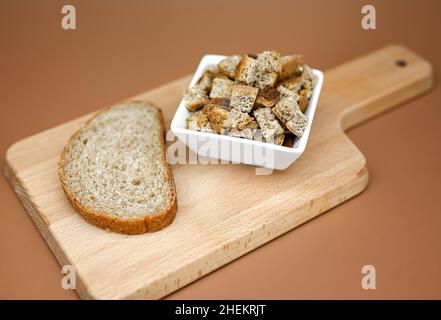 Un pezzo di pane di grano e crostini da esso su un asse di legno. Sfondo beige. Il concetto di estendere la vita dei prodotti a casa, risparmiare. Foto Stock