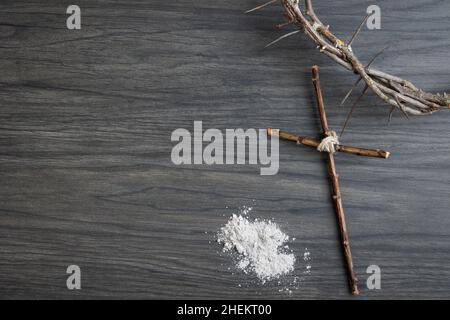 Confine di tenda cristiana con corona di spine, semplice croce di legno e cumulo di ceneri su sfondo di legno scuro con spazio copia Foto Stock