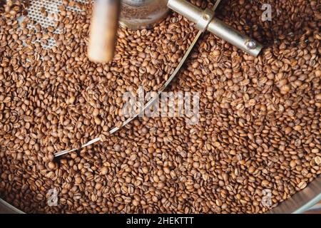 Chicchi di caffè arrosto dopo la tostatura mescolando intorno sulla piastra di raffreddamento del forno. Torrefazione di fagioli industriali. Vista dall'alto Foto Stock