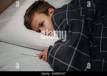 Bambino malato che stesa a letto e che tiene termometro Foto Stock