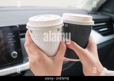 Tazza di carta bianca e bianca con caffè in mani femminili seduti in auto, concetto di Amore e Coppia. Foto Stock