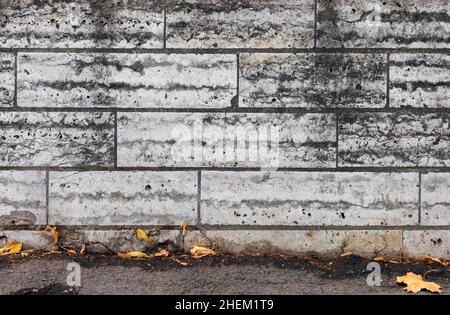 Vecchio muro fatto di pietre grigie e foglie asciutte che posano sul terreno, sfondo foto texture Foto Stock