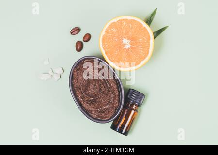 Scrub corpo del caffè cosmetico naturale accanto alla bottiglia di olio essenziale, cristalli di sale marino e arancione fresco, composizione piatta Foto Stock