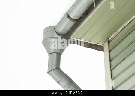 Grondaia ghiacciata in inverno dal tetto al suolo sullo sfondo del muro verde della casa. Tempo freddo Foto Stock