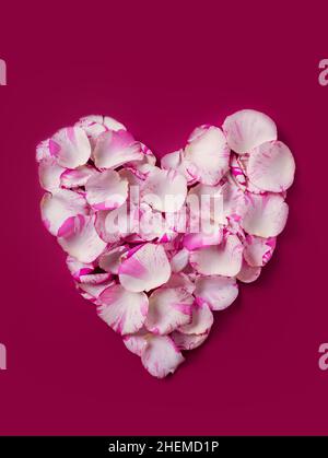 Corona a forma di cuore per le vacanze realizzata con petali di rosa su sfondo rosso, biglietto di auguri per San Valentino o per il giorno di nozze, vista dall'alto Foto Stock