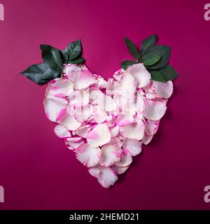 Corona a forma di cuore per le vacanze realizzata con petali di rosa su sfondo rosso, biglietto di auguri per San Valentino o per il giorno di nozze, vista dall'alto Foto Stock