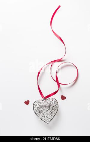 Biglietto di auguri San Valentino, bel cuore d'argento con piccoli cuori rossi con nastro su sfondo bianco Foto Stock