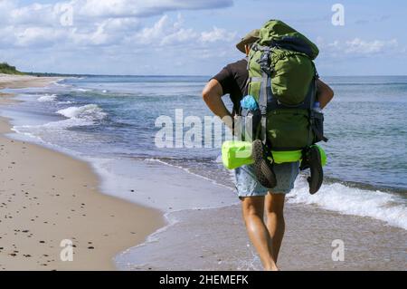 Regione di Kaliningrad, Mar Baltico, Russia, 5 agosto 2021. Un'escursione lungo il litorale. Un uomo con un grande zaino. Un turista cammina lungo la costa del mare Foto Stock