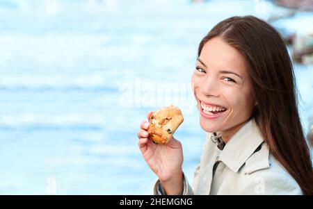 Scone pasticceria Asiatica donna che mangia dolce britannico sul mare ritratto. Giovane modello sorridente a macchina fotografica che tiene cibo da forno Foto Stock