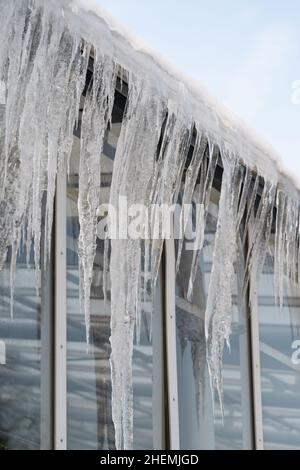 Ghiaccioli appendono dal tetto e dal muro in inverno. Acqua congelata da ghiaccio e neve durante lo scongelamento primaverile Foto Stock