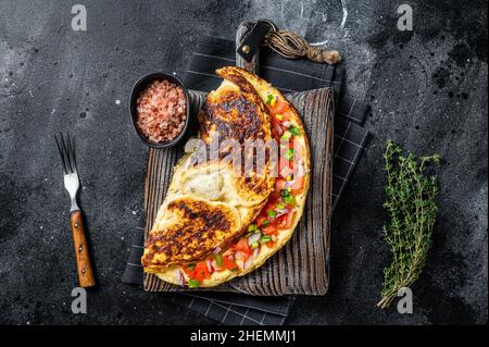 Frittata farcita con pomodori, peperone rosso e cipolla su tavola di legno. Sfondo nero. Vista dall'alto Foto Stock