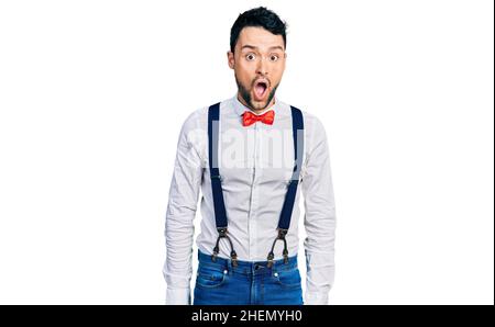 Uomo ispanico con barba che indossa il look hipster con cravatta di prua e sospensori paura e scioccato con espressione di sorpresa, paura e volto eccitato. Foto Stock