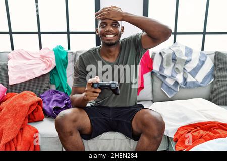 Giovane afroamericano che gioca video gioco seduto sul divano stressato e frustrato con mano sulla testa, sorpreso e faccia arrabbiata Foto Stock