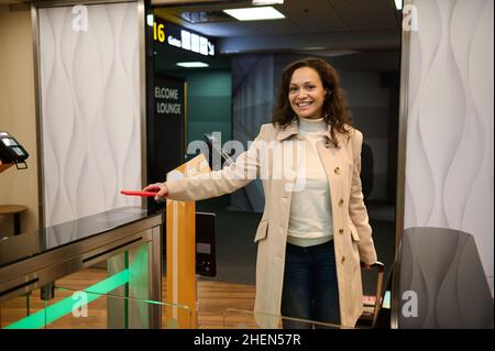 Sorridente passeggero donna graziosa con valigia scansiona le informazioni sul telefono posizionandolo sullo scanner per leggere il codice QR al banco di check-in mentre Foto Stock