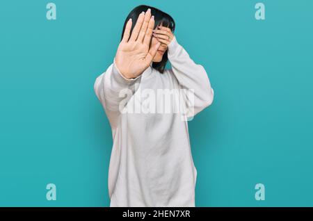 Giovane donna bruna con i bangs che indossano un pullover casual dolcevita coprendo gli occhi con le mani e facendo stop gesture con espressione triste e paura. Embarr Foto Stock