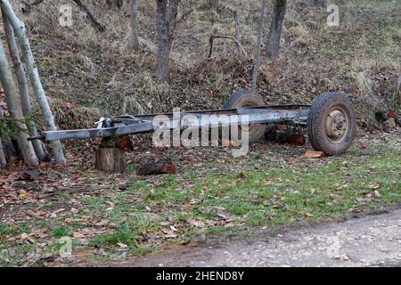 Rimorchio in legno di metallo vuoto fatto a mano parcheggiato su una strada di campagna vicino alla foresta Foto Stock