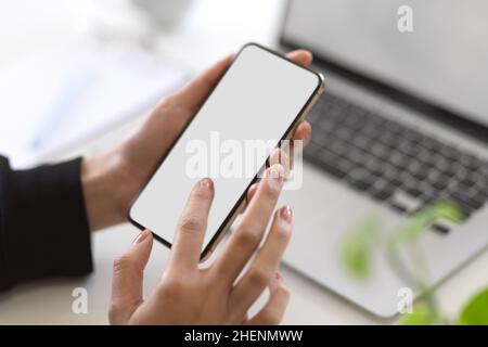 Immagine di primo piano, immagine Mockup di uno schermo vuoto dello smartphone in una scrivania da lavoro con le mani di una donna. Foto Stock