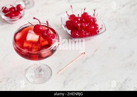 Bicchiere di cocktail Manhattan ghiacciato con ciliegie su sfondo chiaro Foto Stock