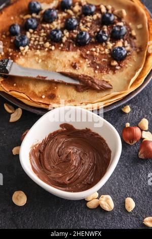 Ciotola con gustosa pasta di cioccolato, noci e crepes su sfondo nero Foto Stock