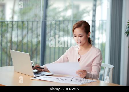 vista laterale di sorridente ragazza asiatica libera che lavora a casa Foto Stock