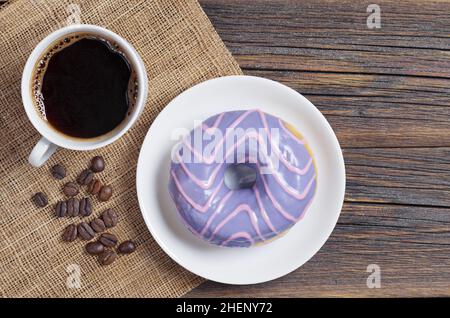 Ciambella con glassa viola e tazza di caffè su vecchio tavolo di legno, vista dall'alto Foto Stock