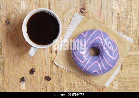 Tazza di caffè e una ciambella con uno smalto viola su un vecchio sfondo di legno, vista dall'alto Foto Stock