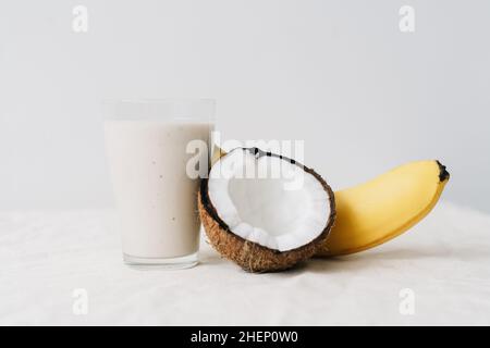 frullato bianco sano fatto di banana e cocco fresco, in un bicchiere di vetro. colazione sana, stile di vita sano Foto Stock