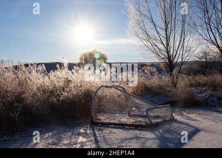 Una rete di hockey viene posata su un laghetto ghiacciato mentre il sole del mattino splende su un paesaggio ghiacciato. Foto Stock