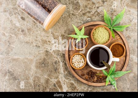 una tazza di caffè nero biologico, foglie di morijuana e semi su un vassoio di legno rotondo vista dall'alto. CBD Foto Stock