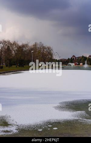 Lago artificiale parzialmente congelato e fontana in un parco cittadino Foto Stock