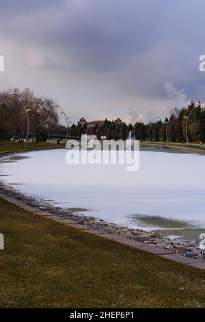 Lago artificiale parzialmente congelato e fontana in un parco cittadino Foto Stock