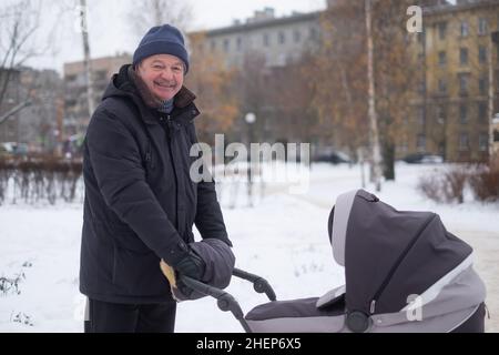 Nonno che cammina con un passeggino in inverno nevoso Foto Stock