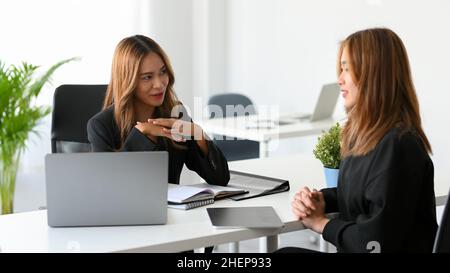 Una donna attraente manager intervista la sua candidata di lavoro in ufficio. Le risorse umane intervistano un candidato. Concetto di colloquio di lavoro. Foto Stock